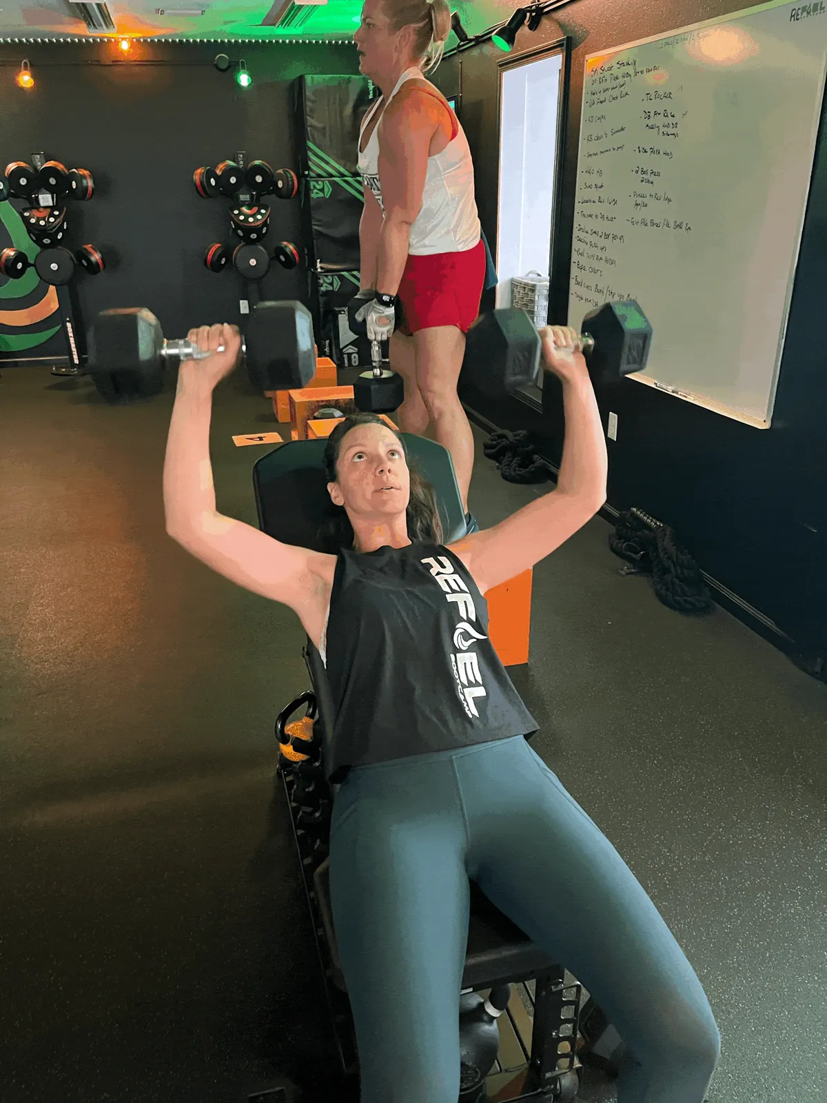 Member pressing dumbbells during a strength class